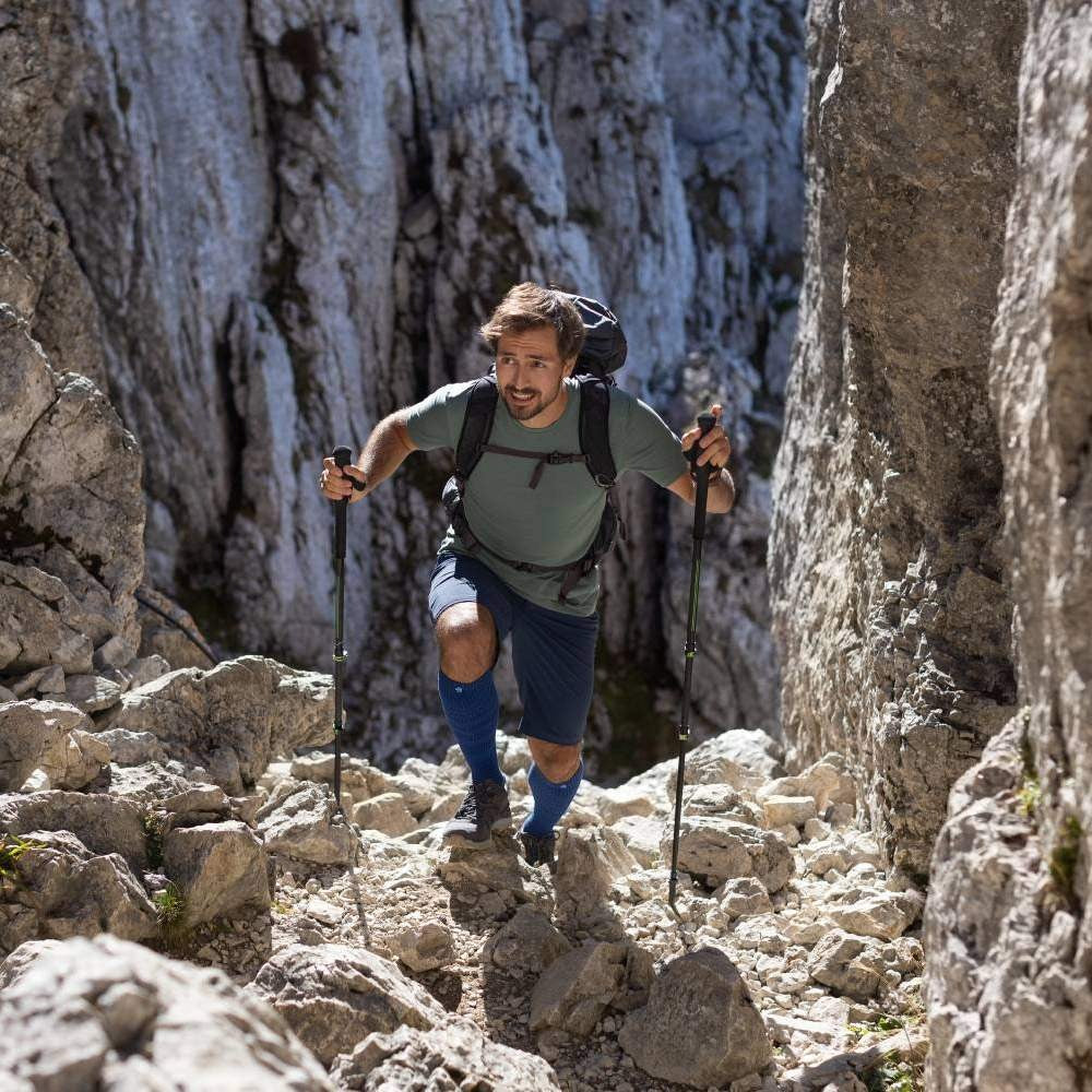 Man hiking through a rocky mountain pass with backpack and trekking poles.