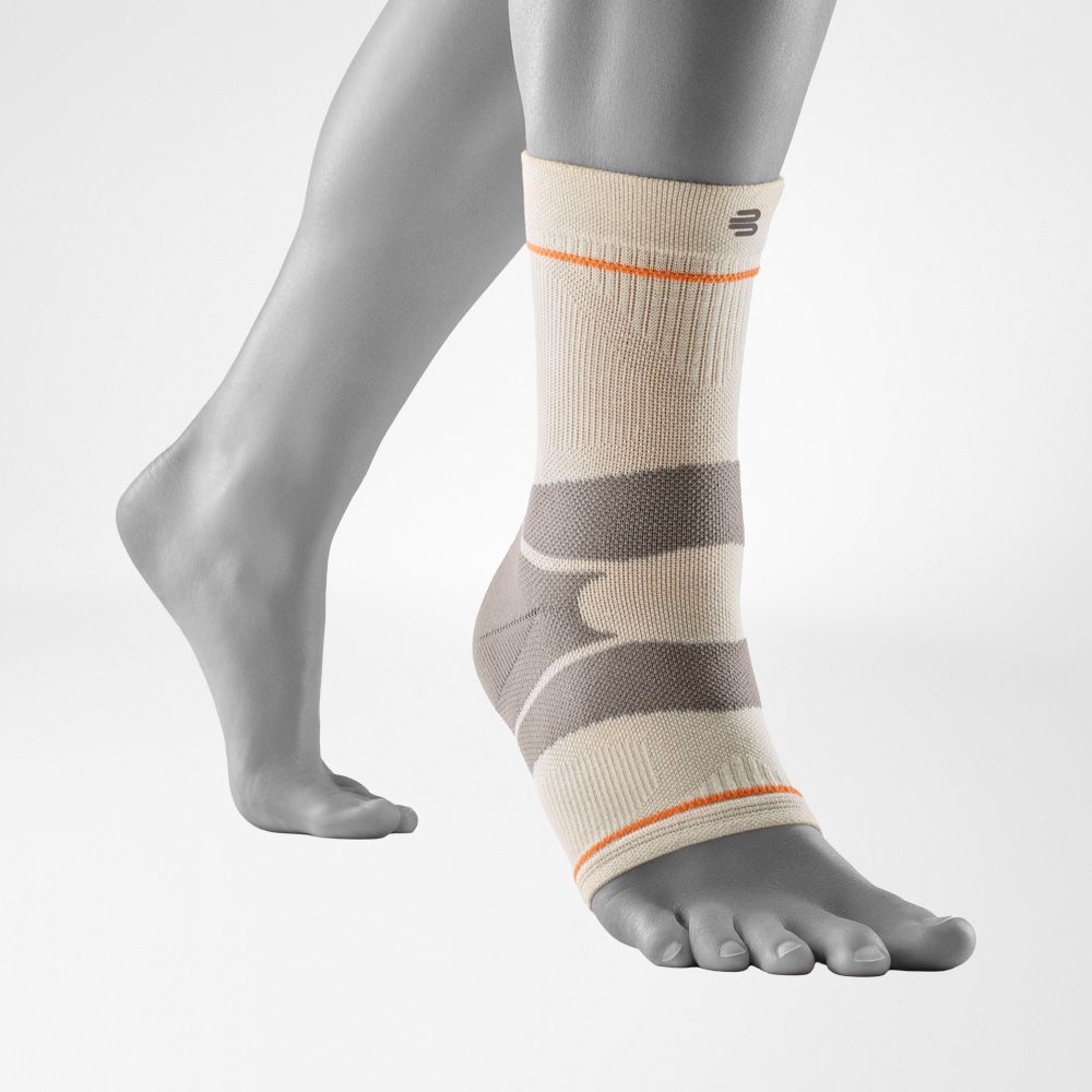 A close-up of a person's ankle wearing a Bauerfeind Sports outdoor ankle compression sleeve with a light gray background.
