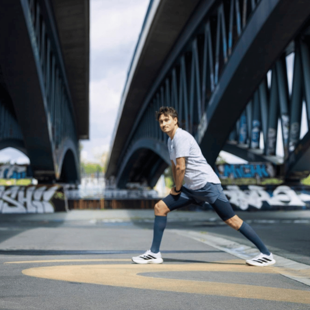 Man stretching on a road with a bridge in the background wearing bauerfeinds navy run ultralight compression socks.