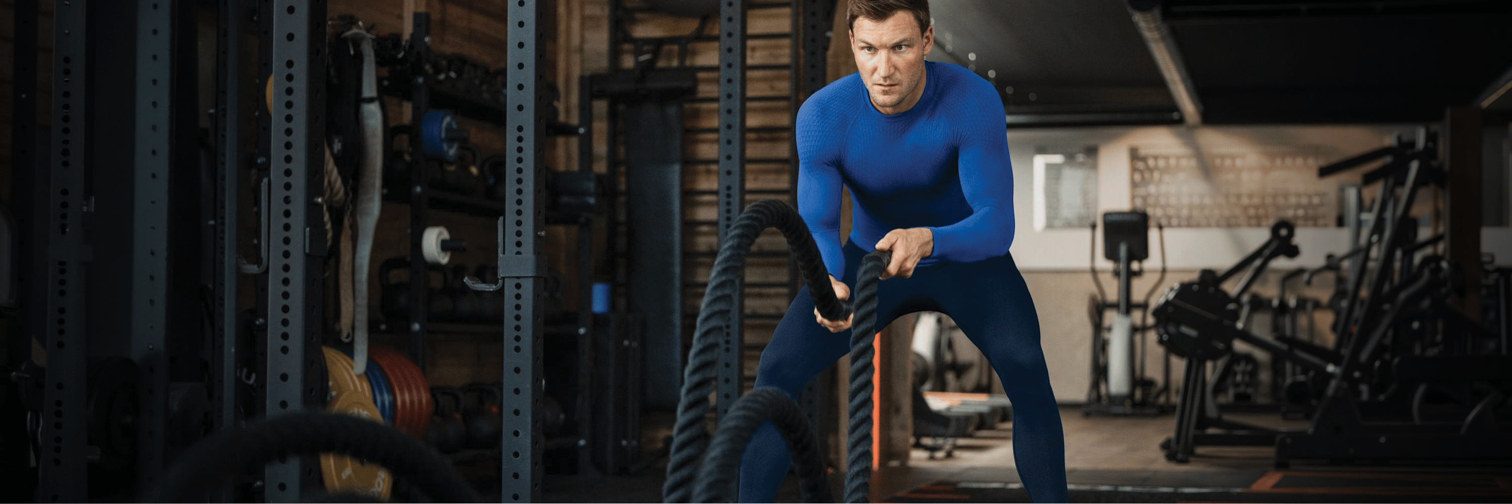 A man in bauerfeind sports compression wear performing battle ropes in a gym setting.