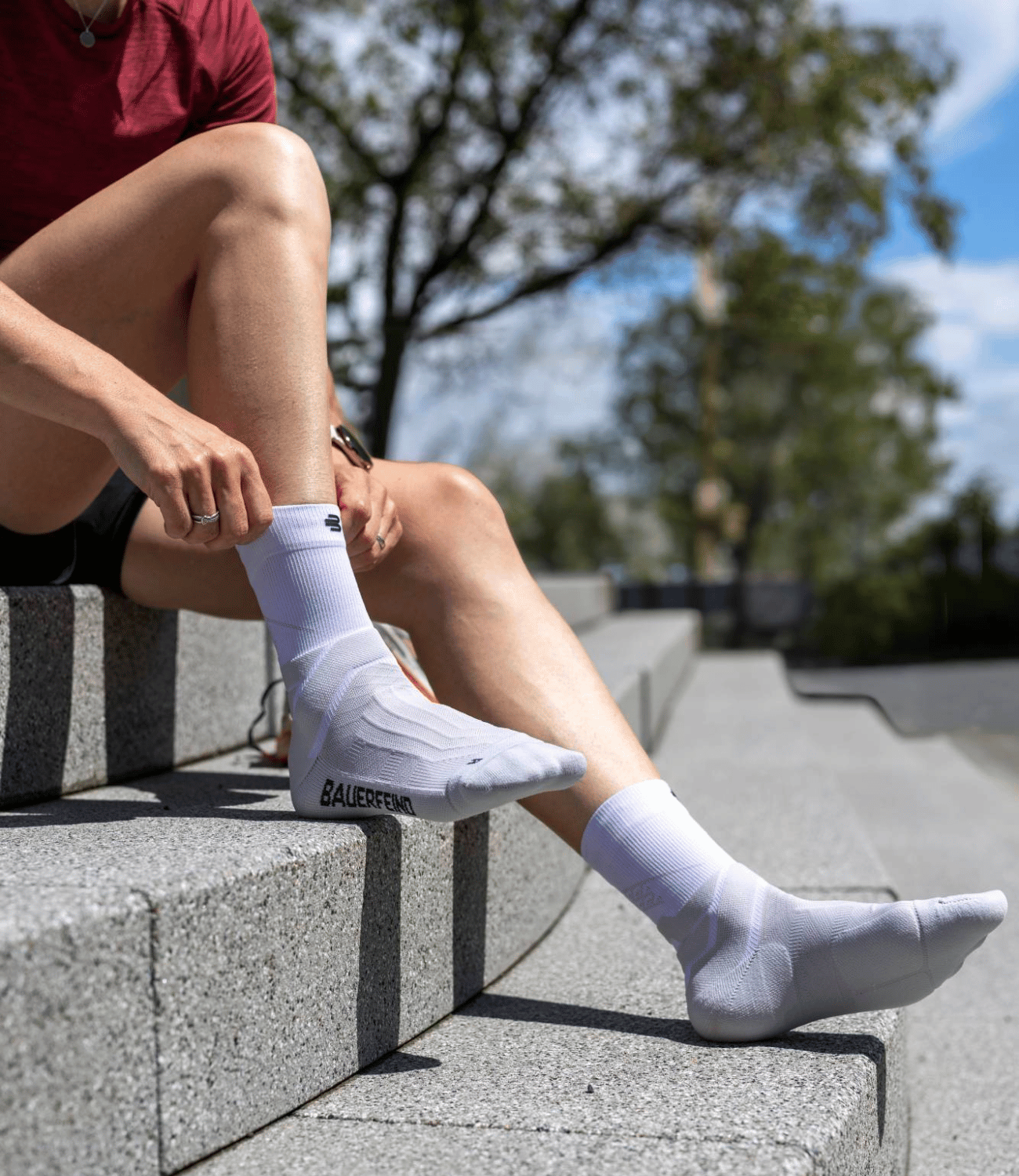 Person pulling up their white mid-cut bauerfeind run performance compression socks on cement steps.