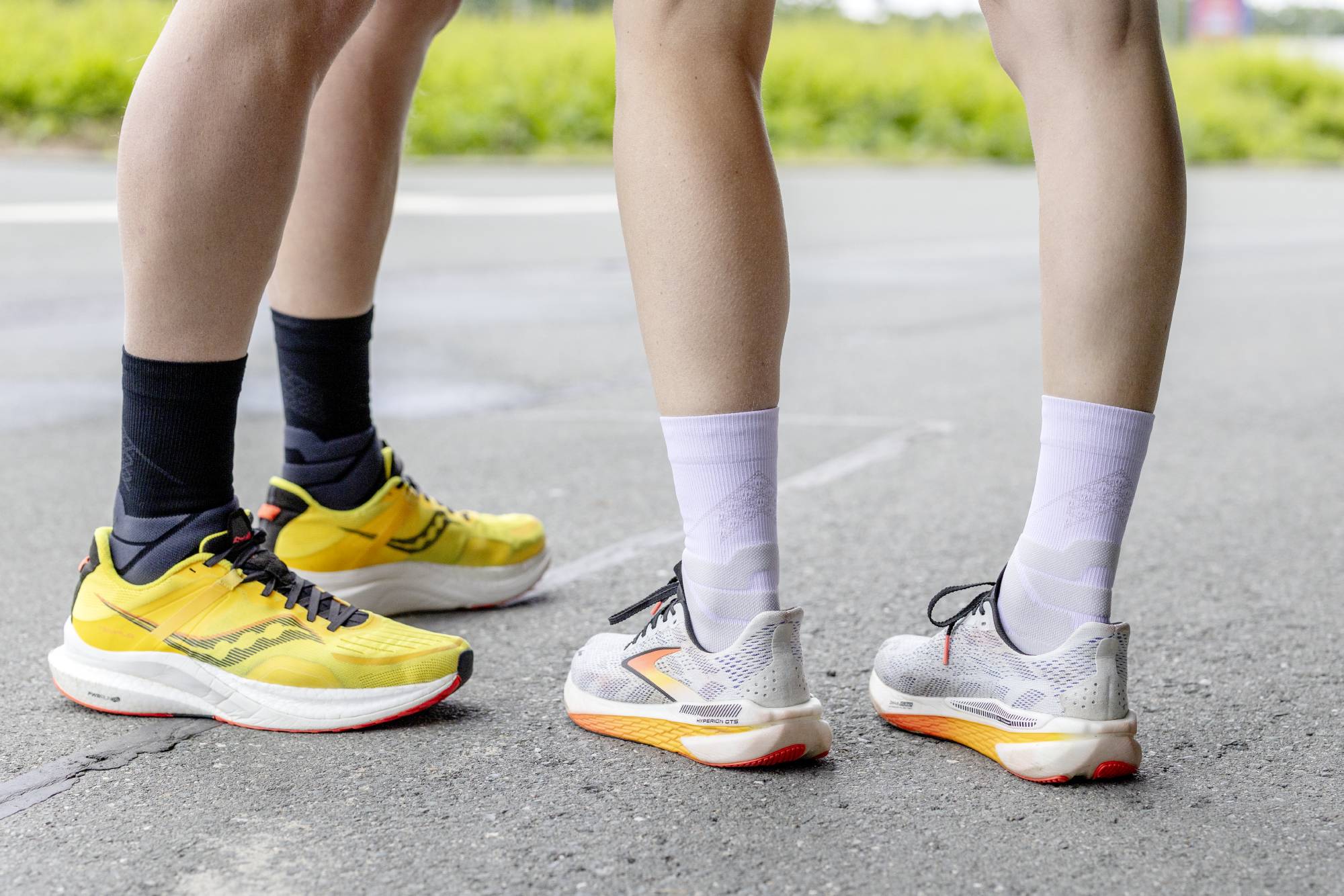 Two people wearing Black and white bauerfeind mid-cut run performance compression socks wearing different colored running shoes on a road.