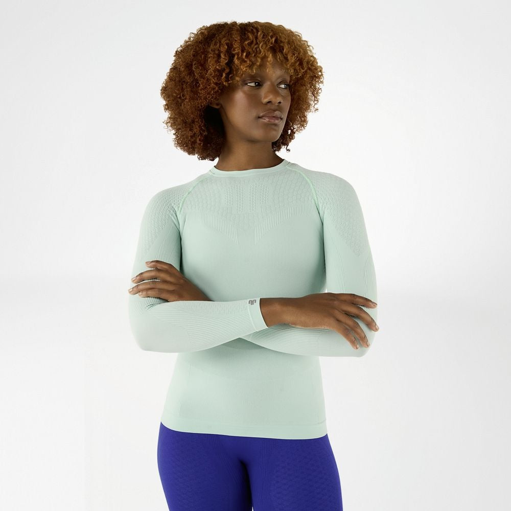 Woman wearing a mint bauerfeind compression long-sleeve top and blue compression leggings on a white background