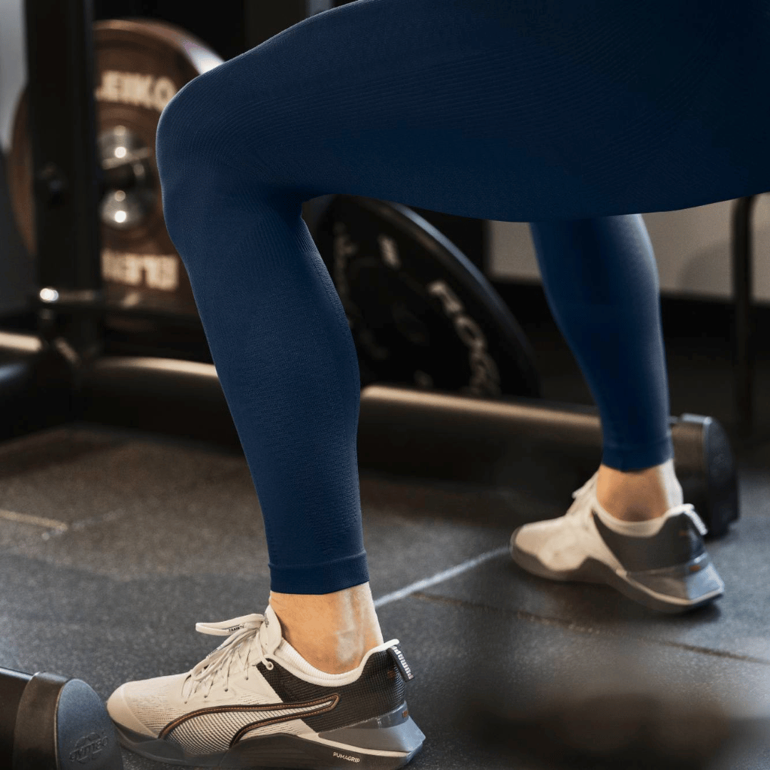 Person wearing blue bauerfeind compression leggings and white sneakers in a gym setting
