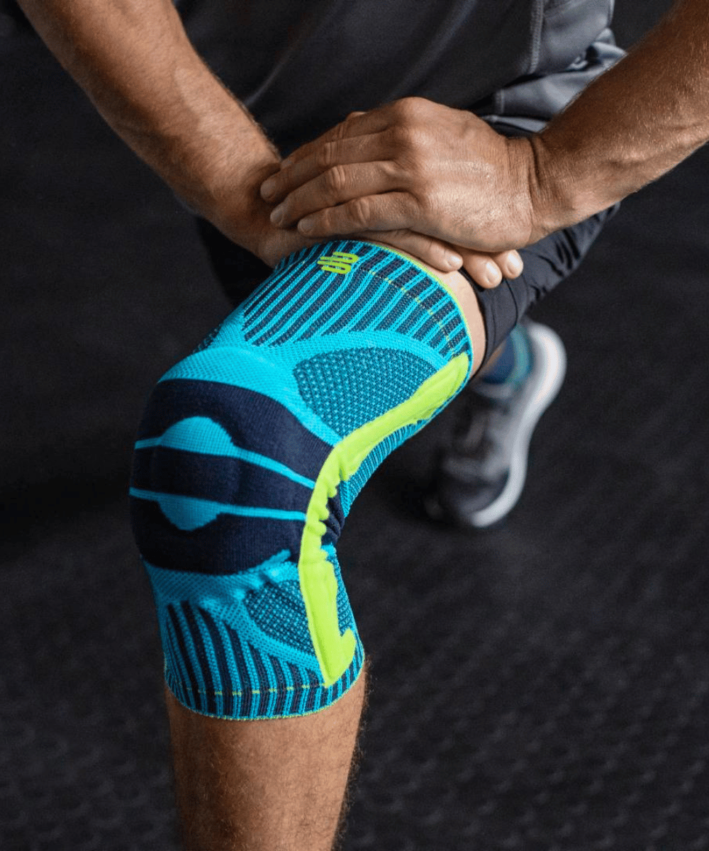 Person wearing a blue and green knee brace on a dark background