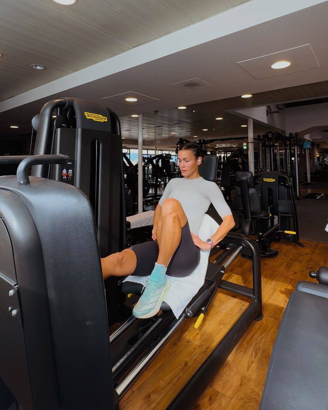 Person in athletic Bauerfeind Grey Women's sport compression shorts and in light grey silver Bauerfeind Women's sport compression short sleeve shirt, using a leg press machine in a gym setting