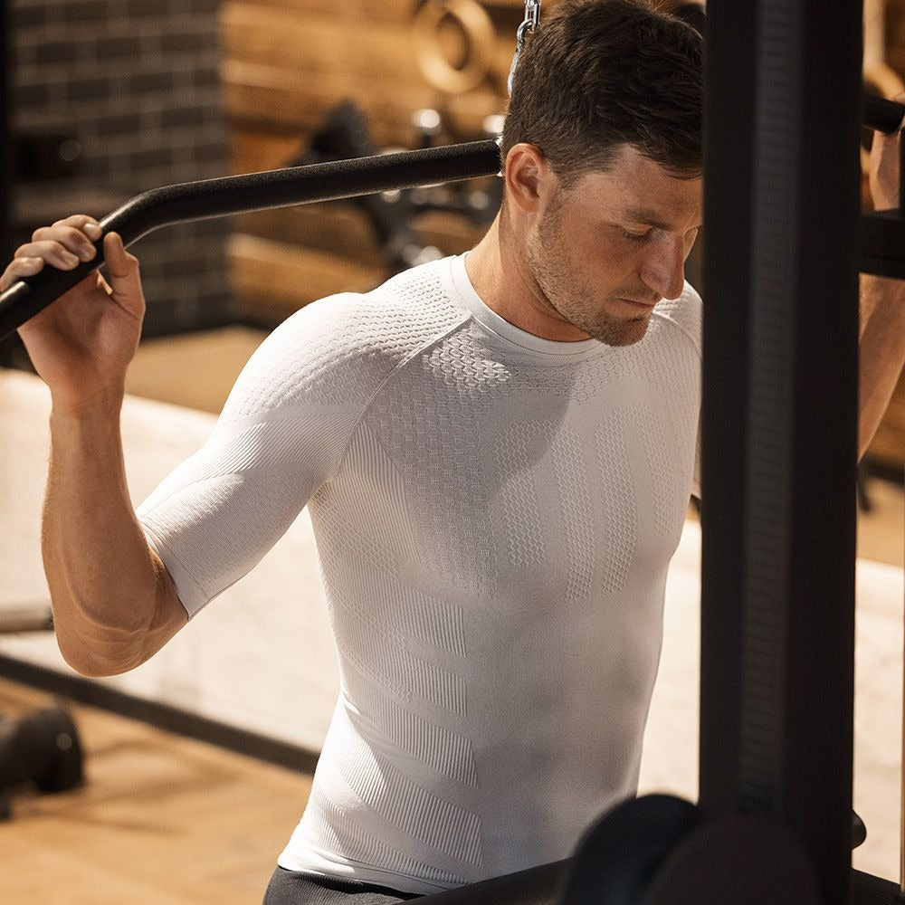 Man exercising in a gym setting wearing a light grey silver Bauerfeind men's sport compression short sleeve shirt