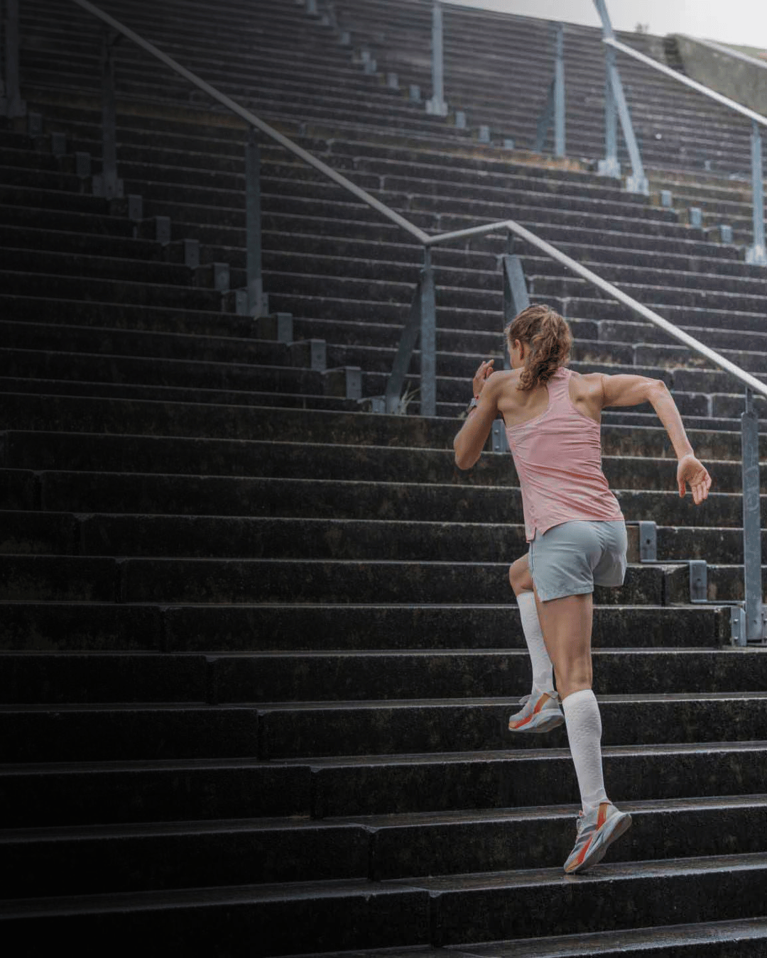 Person running up a set of outdoor stairs wearing bauerfeinds white knee high run performance compression socks in white
