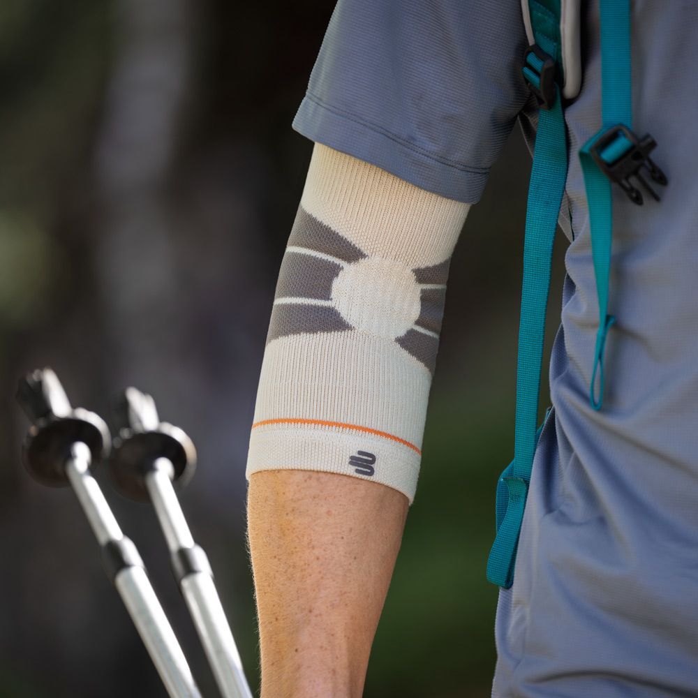 A close-up of a person's arm wearing a Bauerfeind Sports outdoor elbow compression sleeve while on a hike.
