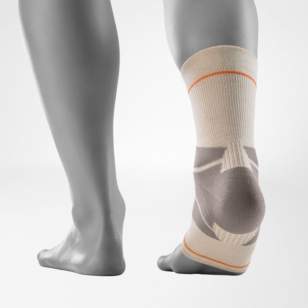 A close-up of a person's ankle wearing a Bauerfeind Sports outdoor ankle compression sleeve with a light gray background.