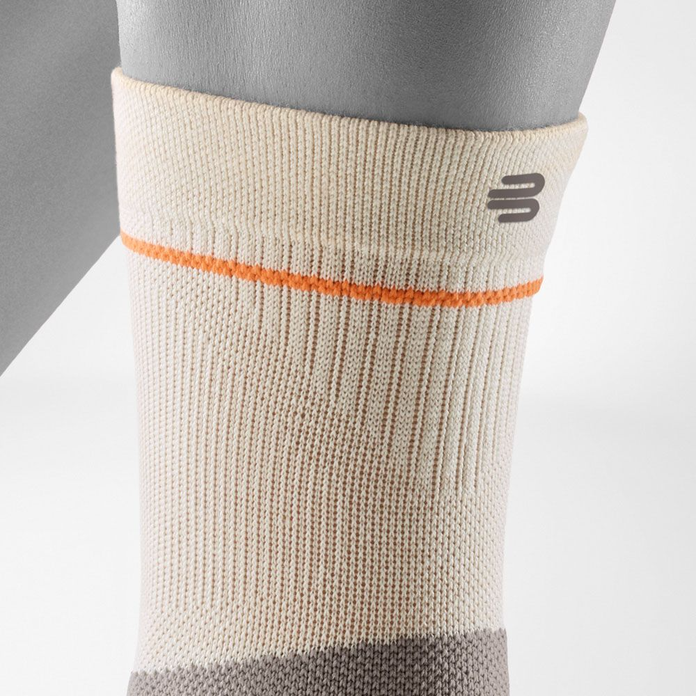 A close-up of a person's ankle wearing a Bauerfeind Sports outdoor ankle compression sleeve with a light gray background.