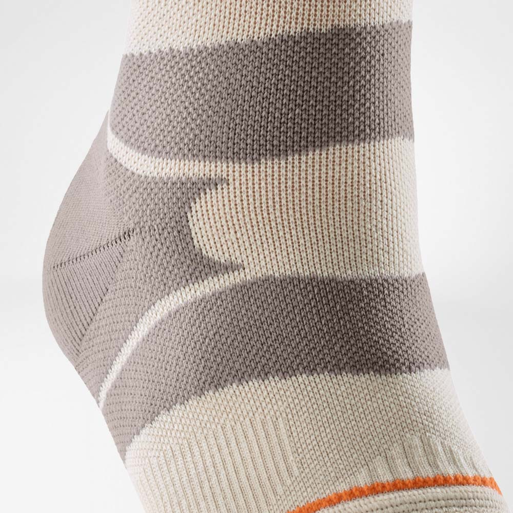 A close-up of a person's ankle wearing a Bauerfeind Sports outdoor ankle compression sleeve with a light gray background.