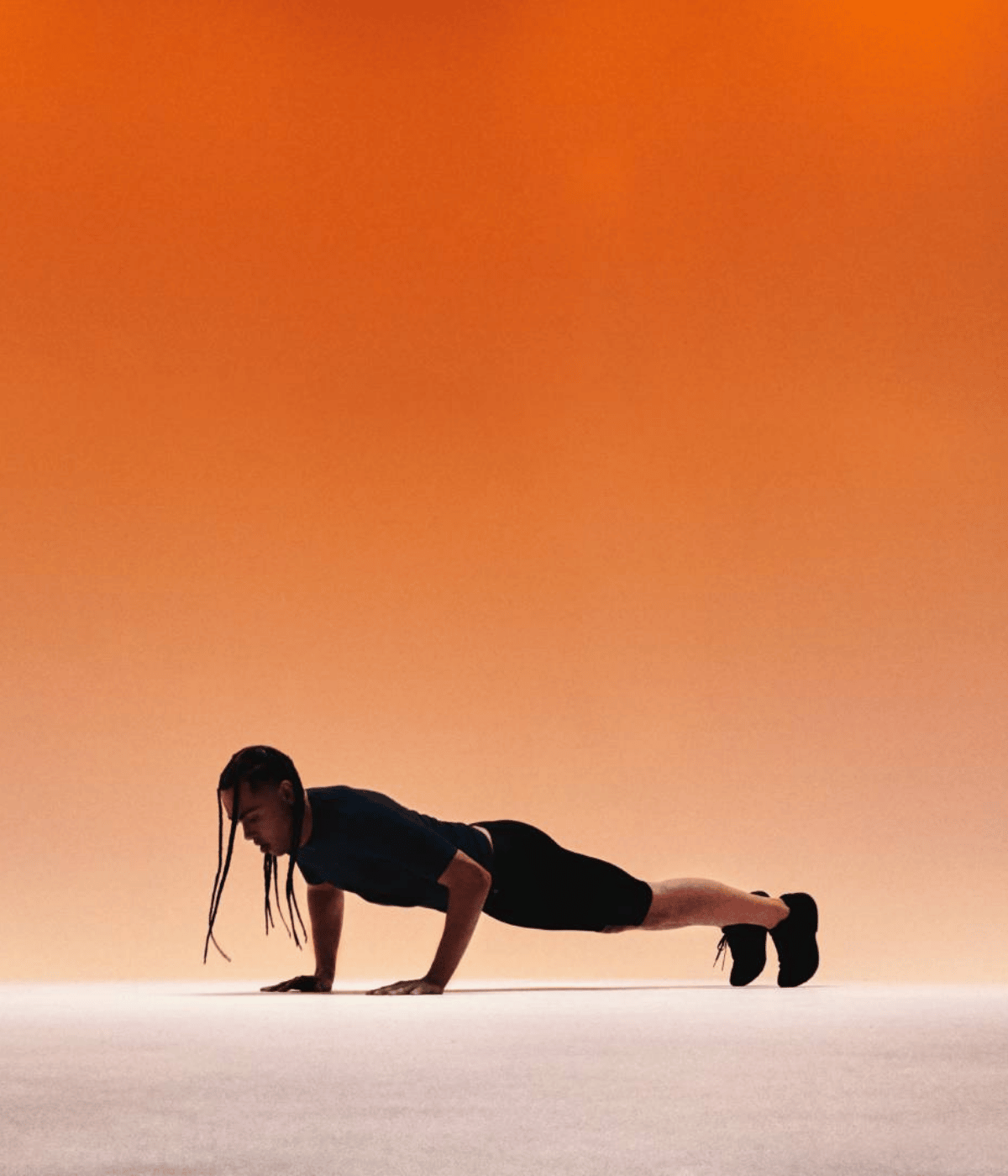 Person in a plank position on a white surface with a gradient orange background while wear Bauerfeind sports compression wear collection