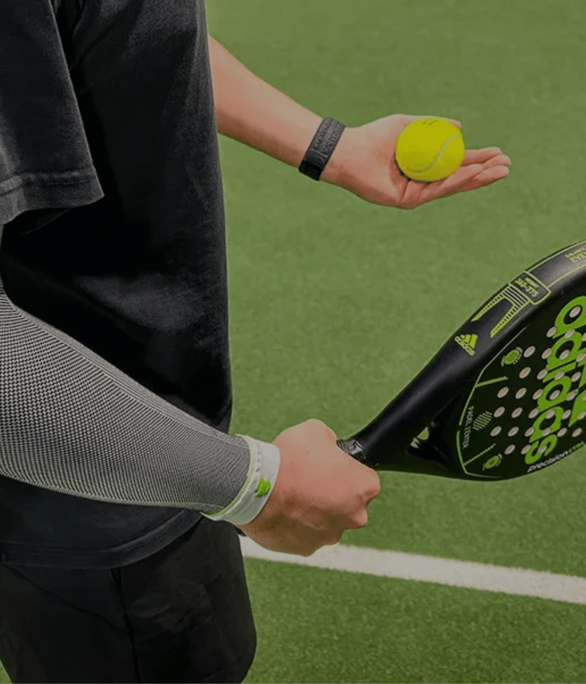 Person holding a racket and a yellow ball on a green court wearing bauerfeind compression sleeve