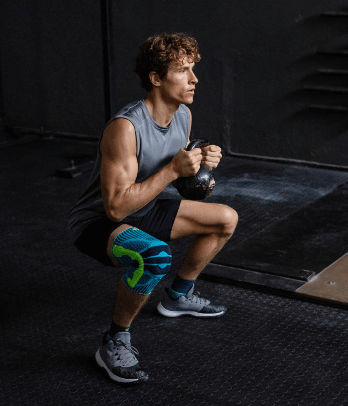 Person exercising with a kettleball in a gym setting wear the Bauerfeind Sports Knee Support.