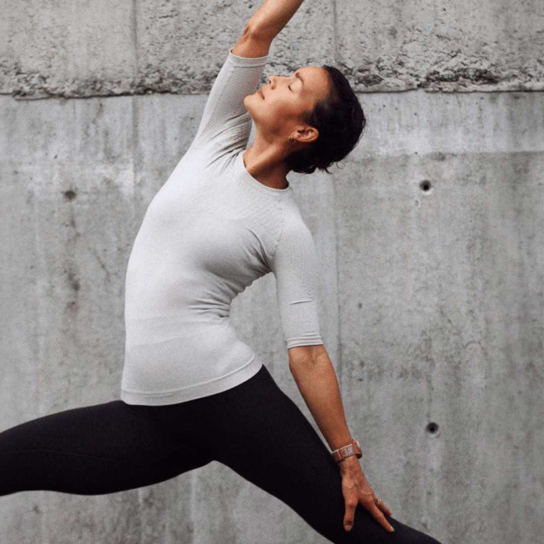 Person in the SILVER bauerfeind's sport compression short shirt and grey bauerfeind's sport compression leggings stretching against a concrete wall