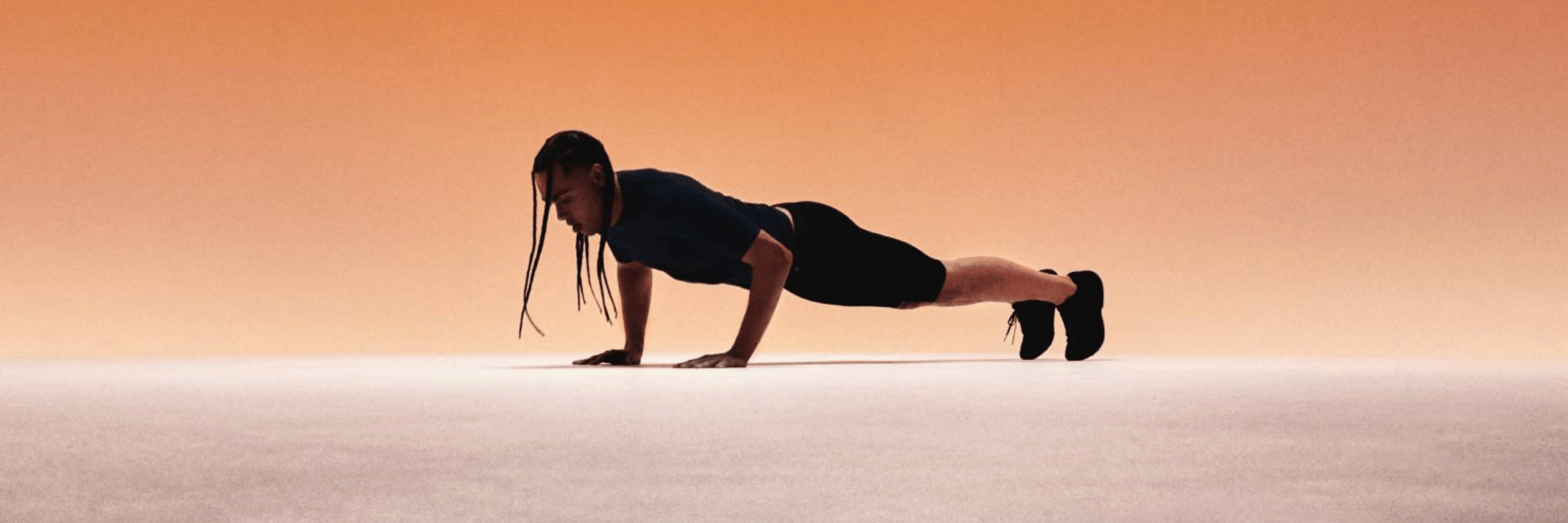 Person in a plank position on a white surface with a gradient orange background while wear Bauerfeind sports compression wear collection