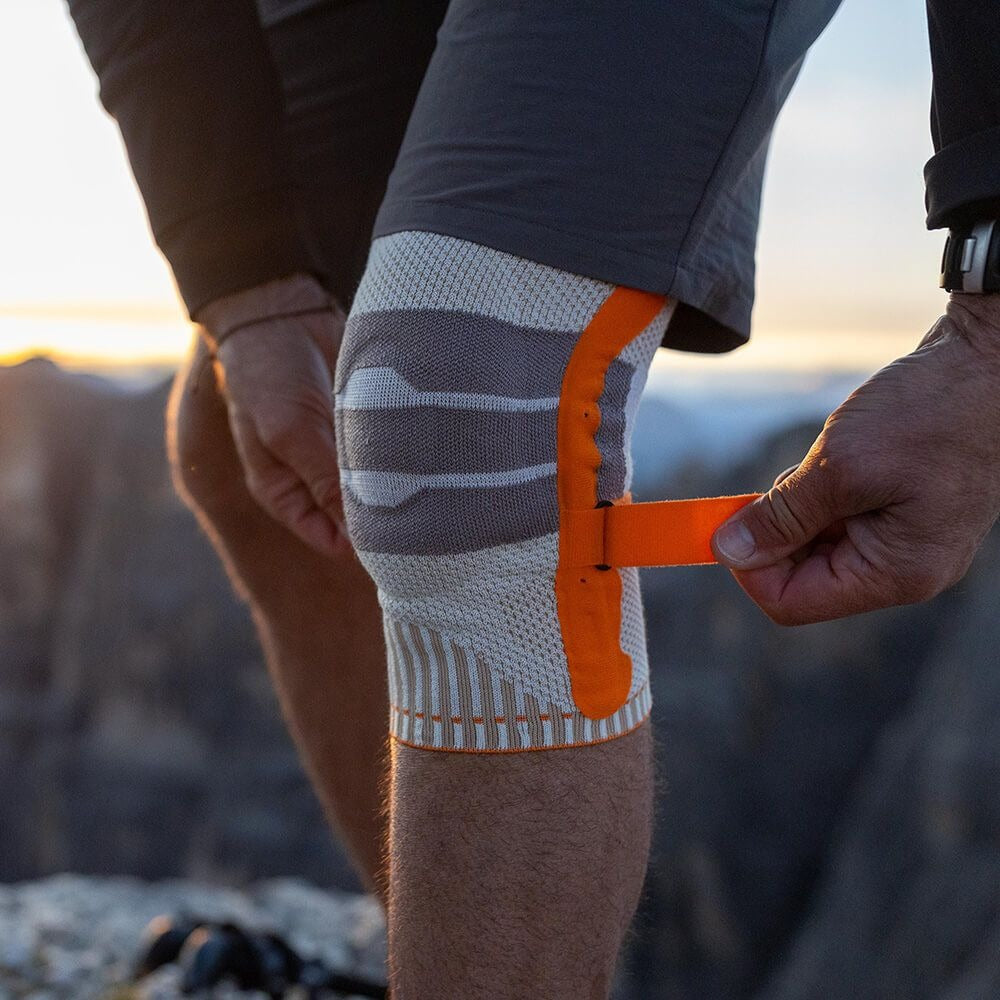 Person applying a knee brace with an orange strap outdoors