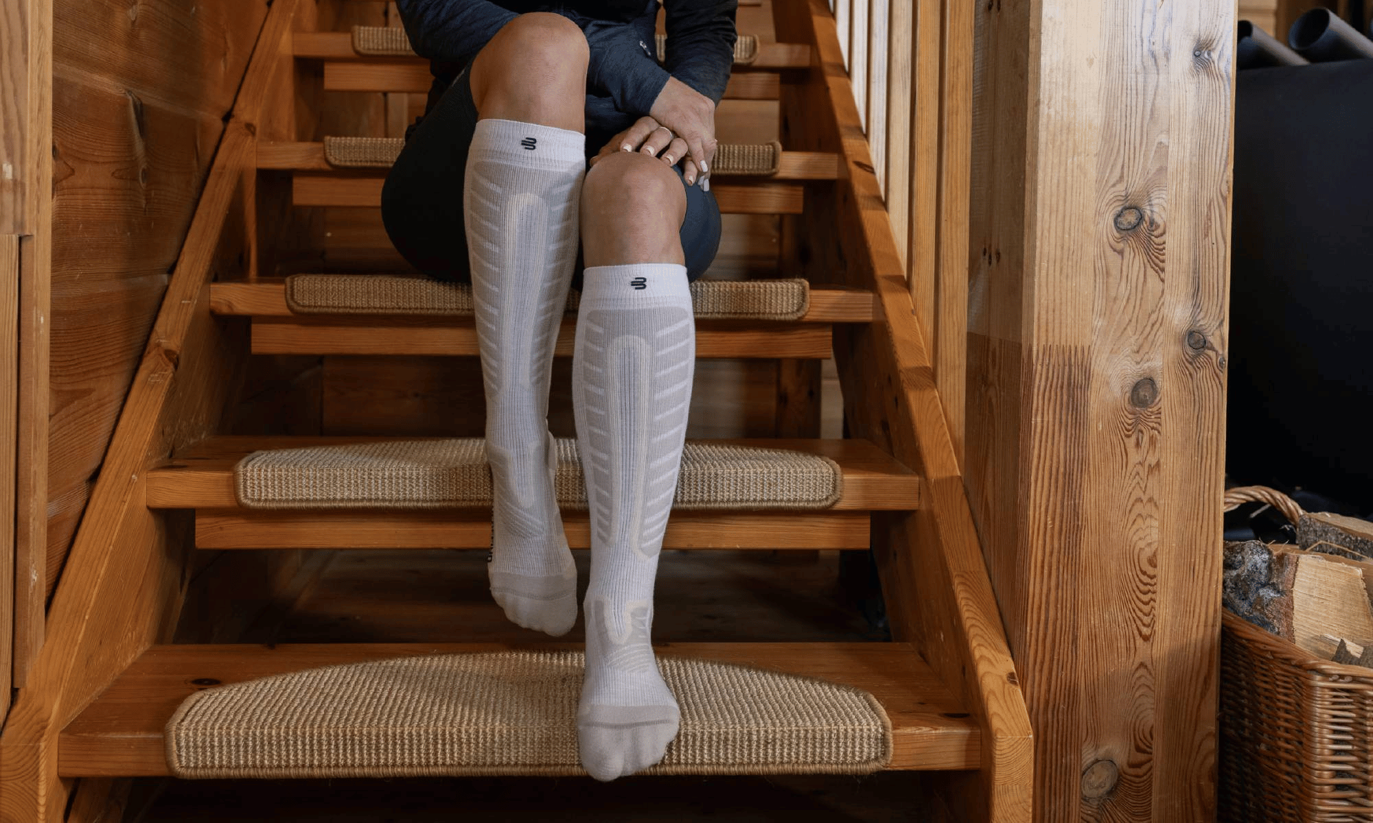 Person wearing knee-high bauerfeind Alpine Ski Compression socks on a wooden staircase