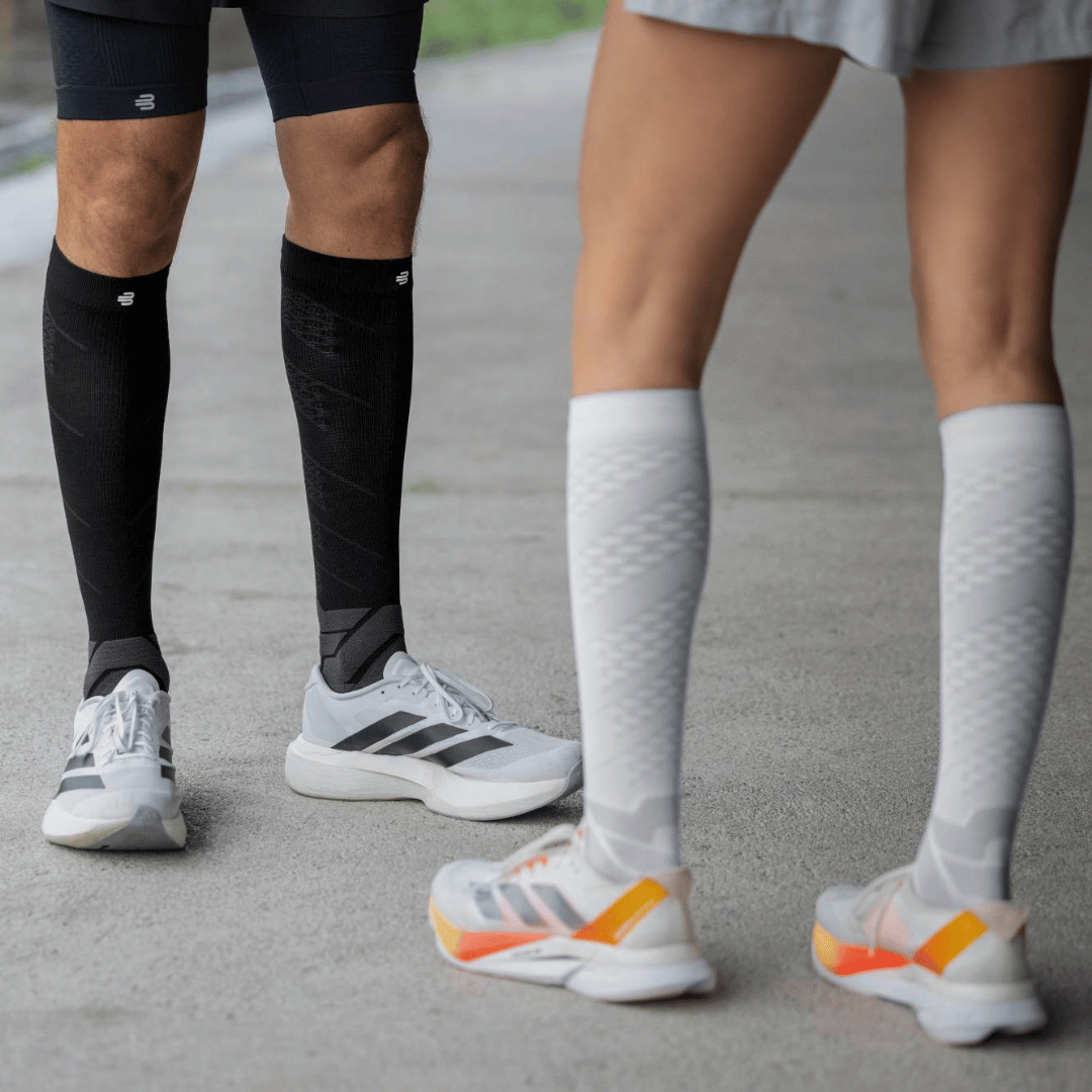 Two people wearing Bauerfeind knee high performance run compression socks in black and white and running shoes on a road. 