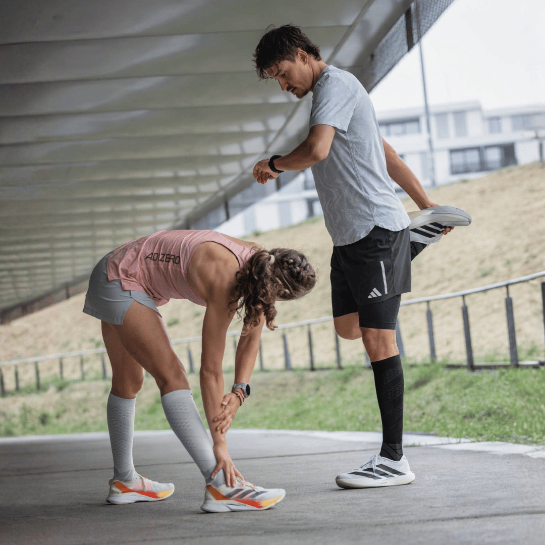 Two people stretching outdoors on a path before a run while wearing black and shite Bauerfeind Performance Run Compression Socks