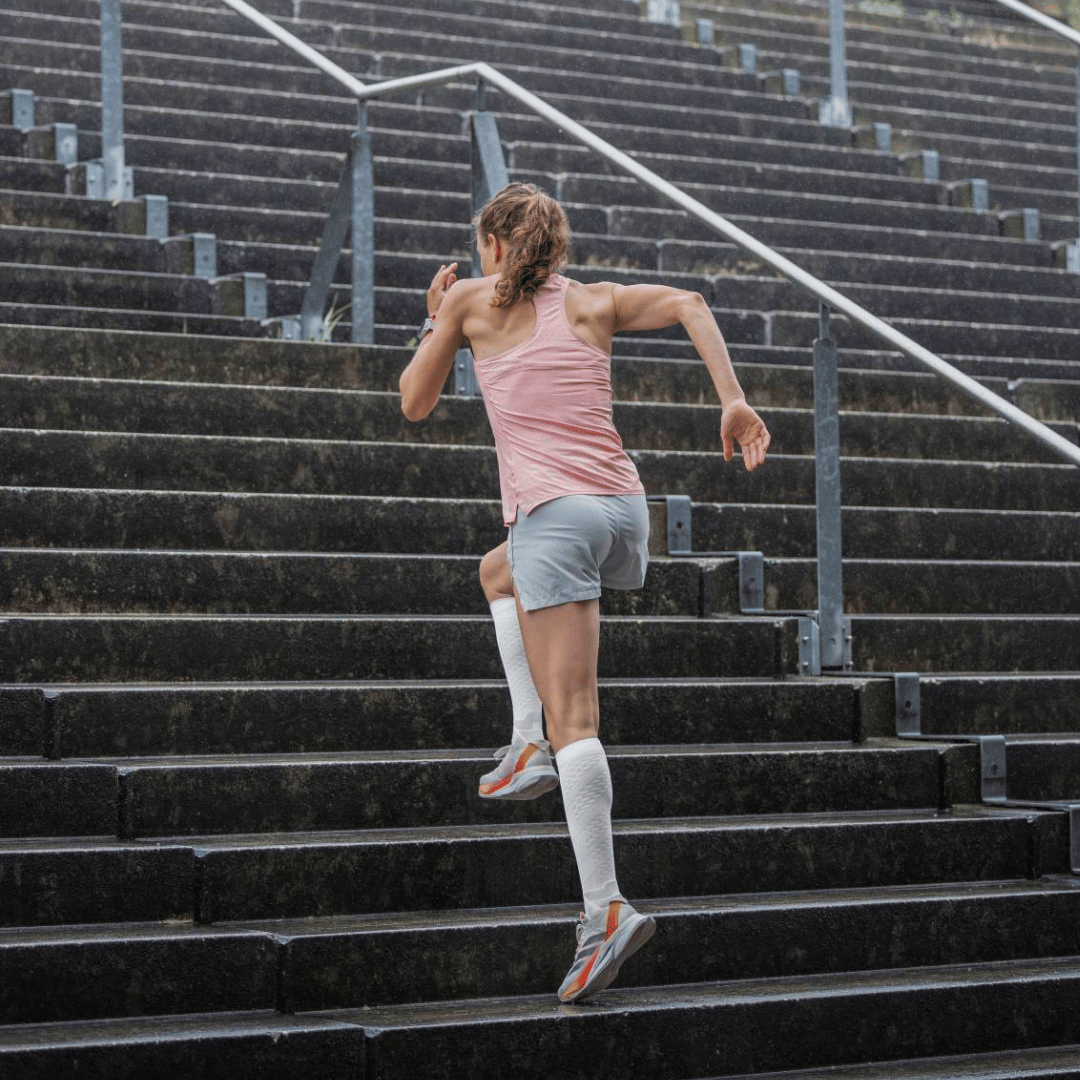 Person running up a set of outdoor stairs while wearing white Bauerfeind knee high Performance run compression socks