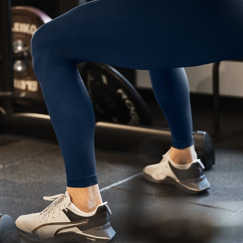 Man wearing blue bauerfeind compression leggings and white sneakers in a gym setting