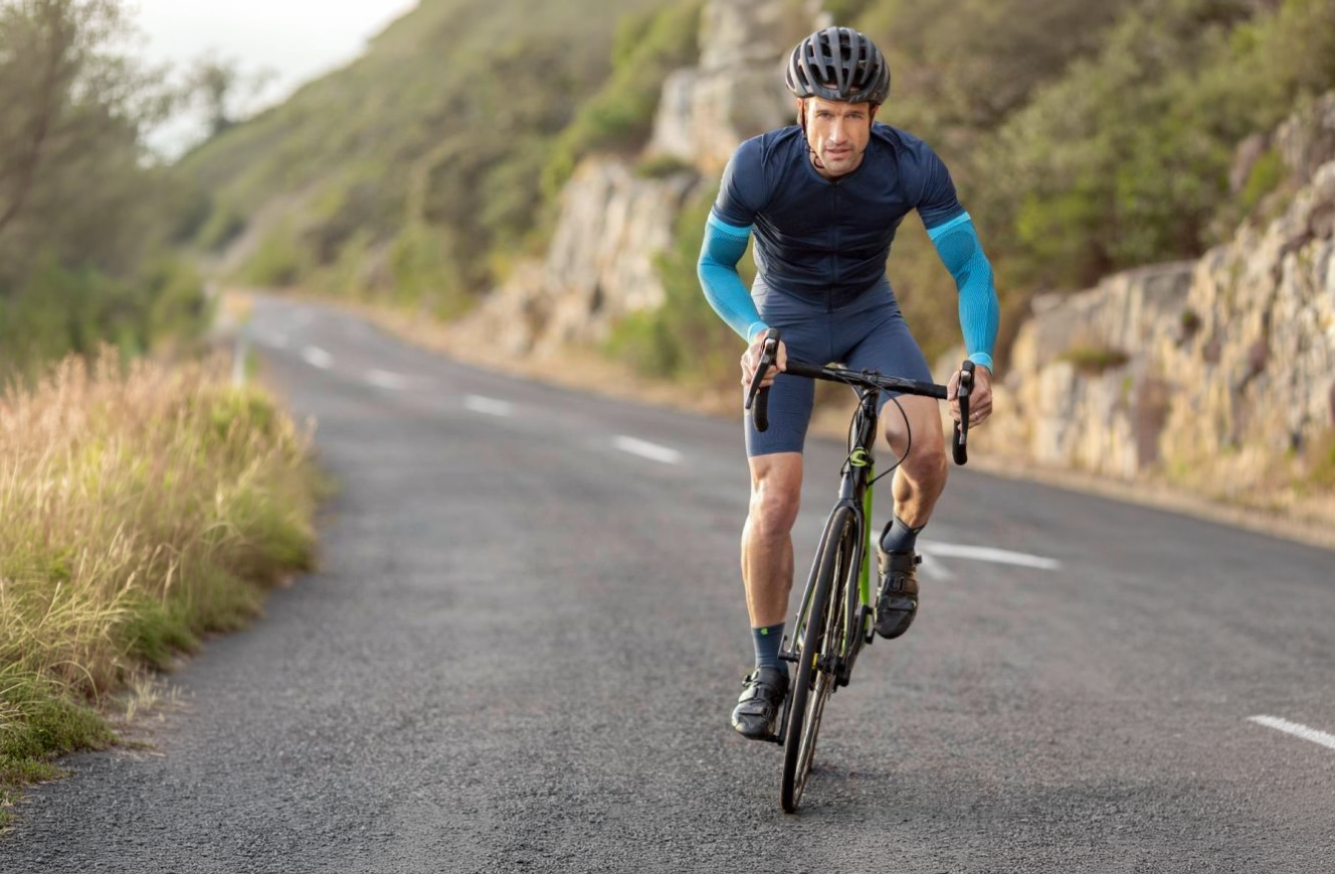Cyclist riding on a road wearing bauerfeind sports compression arm sleeve with a mountainous landscape in the background