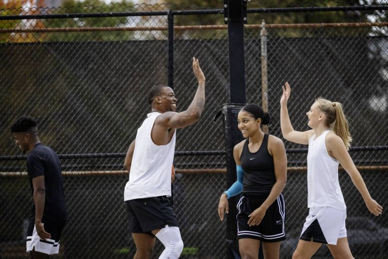 Group of people on a basketball court with one person giving a high-five. Guy wearing the black bauerfeind Sports Knee Support NBA and a woman wearing bauerfeind sports compression arm sleeve