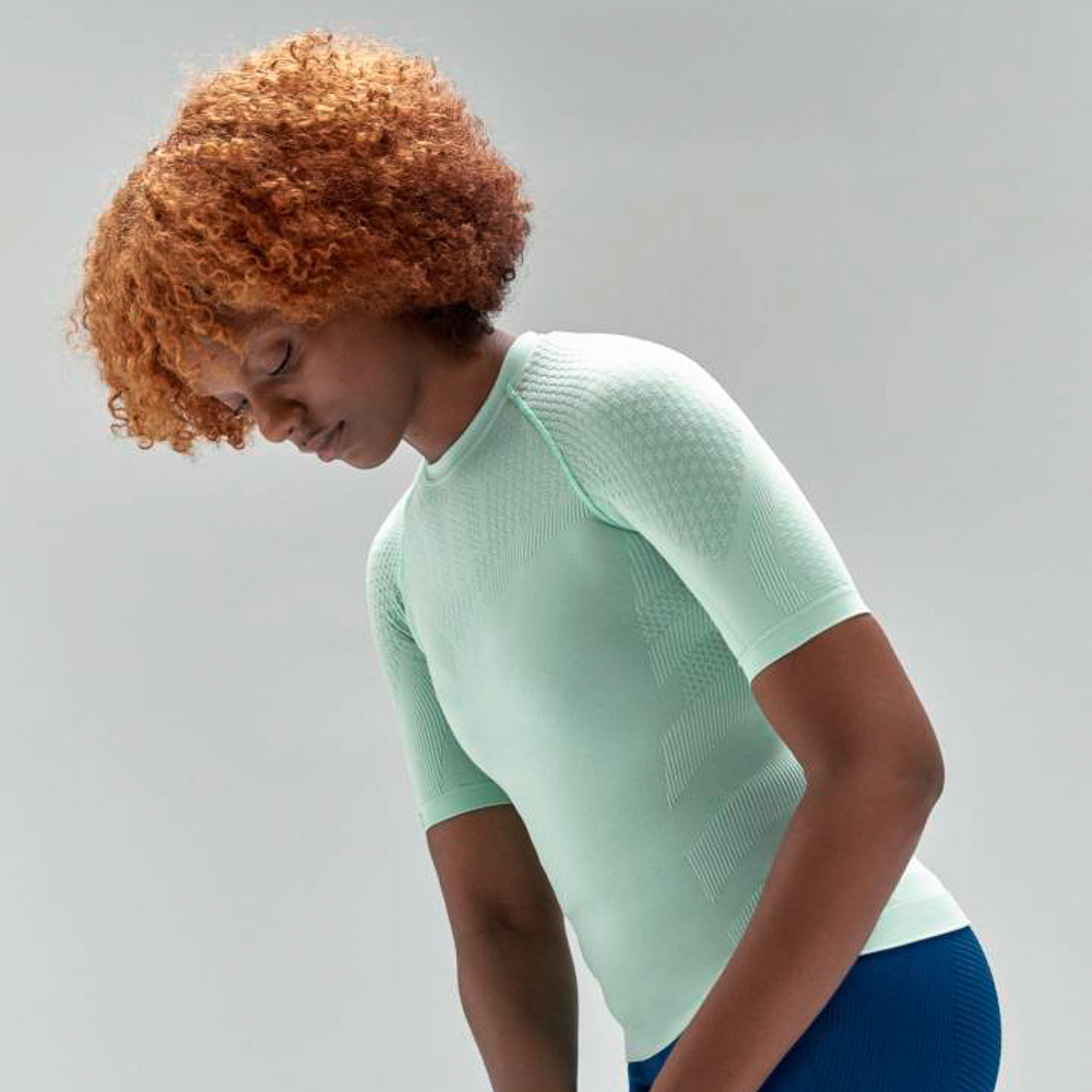 Woman wearing a mint Bauerfeind sport women's compression short sleeve shirt and bauerfeind compression blue shorts on a gray background