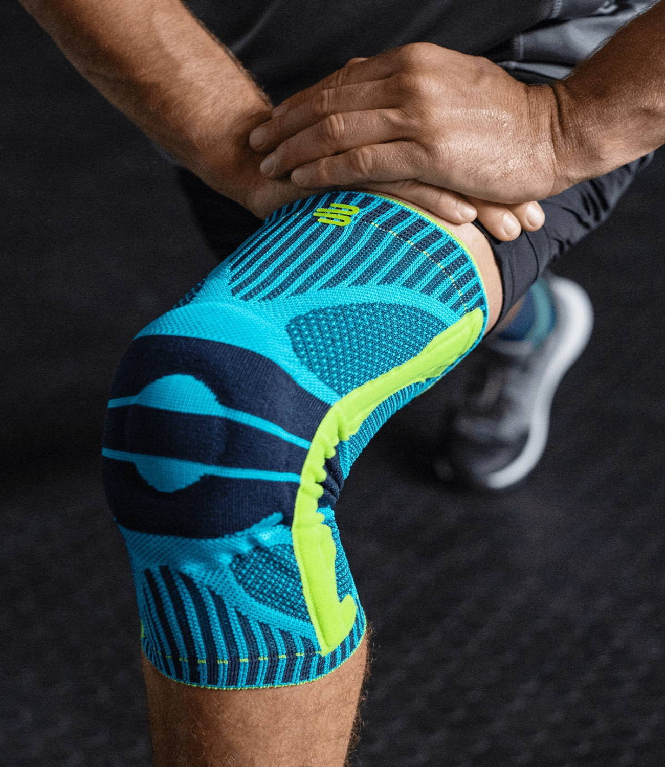 Person wearing a blue and green knee brace on a dark background