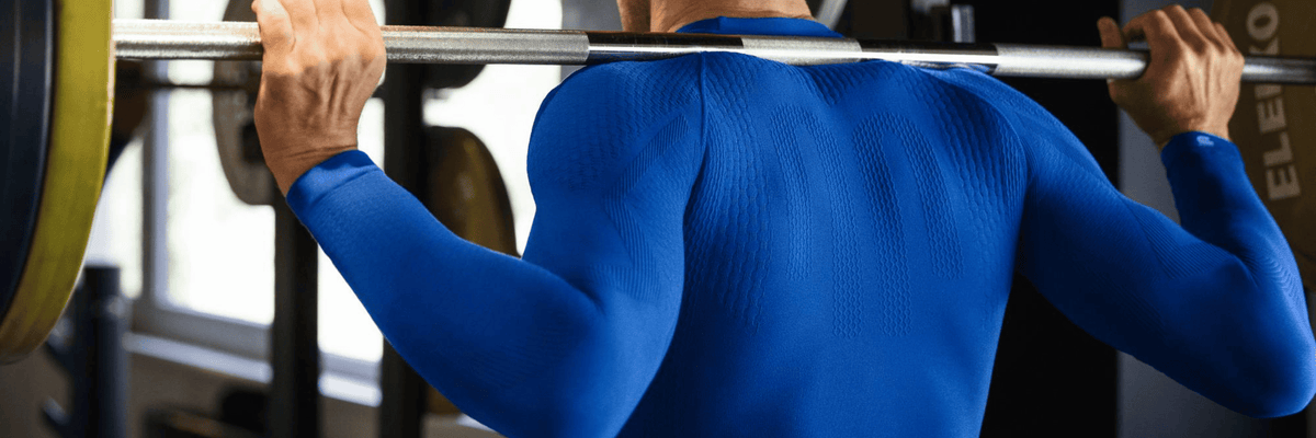 Person wearing blue bauerfeind compression shirt long sleeve lifting a barbell in a gym setting