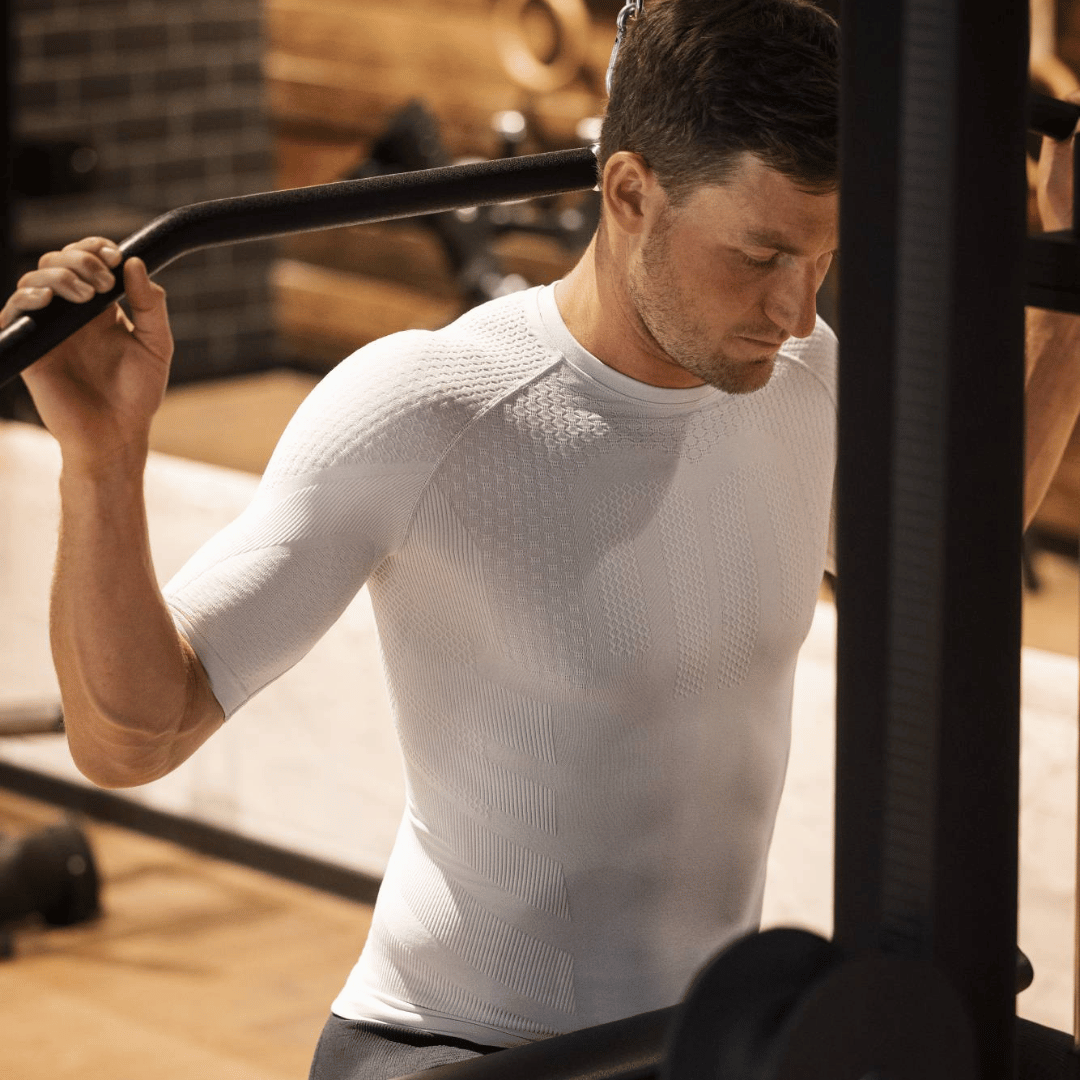 Man exercising with a barbell in a gym setting wearing bauerfeind sports white compression t-shirt