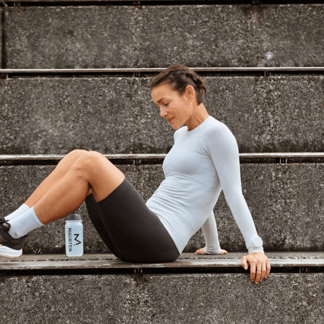 Woman exercising on concrete steps with a water bottle nearby wearing grey athletic Bauerfeind Women's sport compression shorts