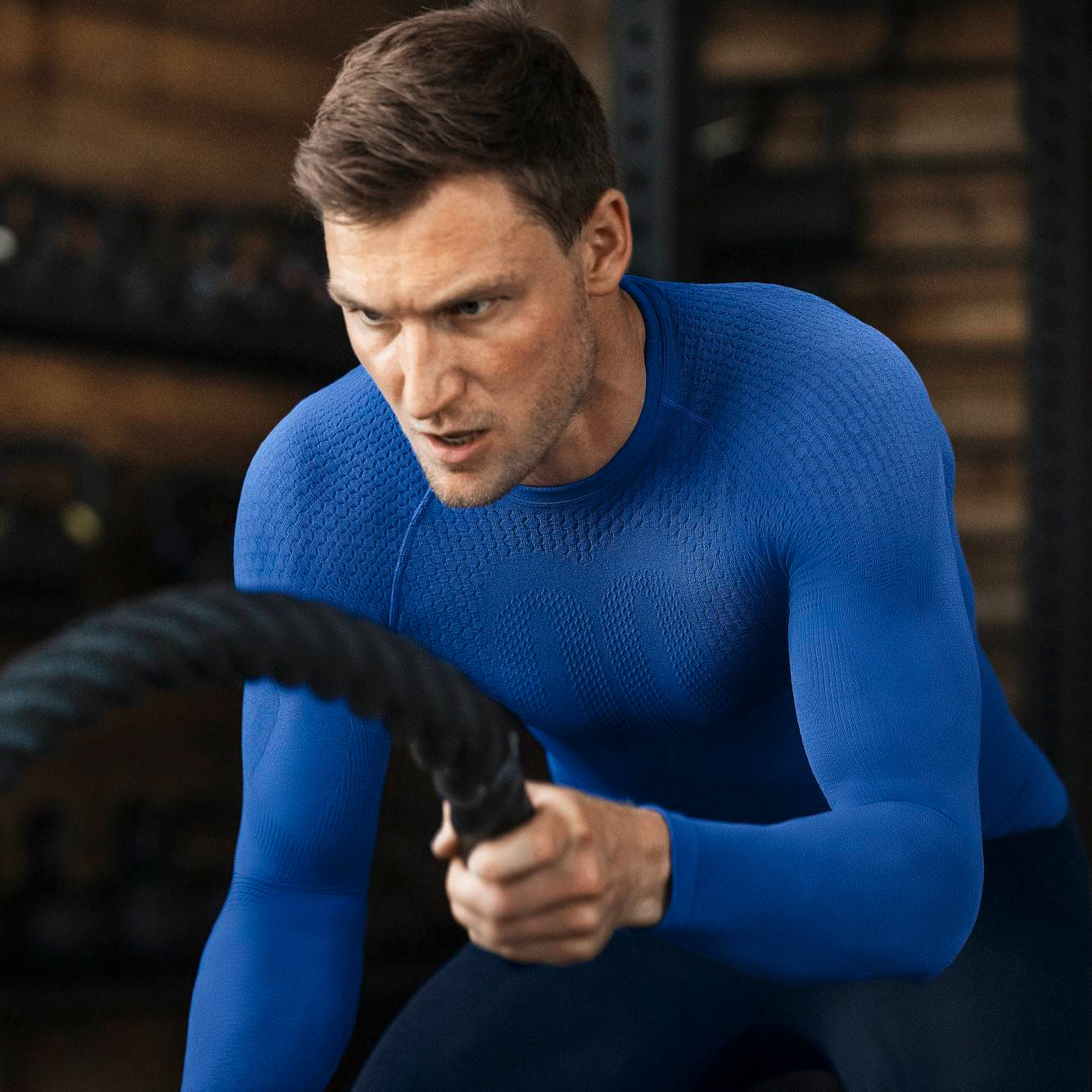 Man in a blue bauerfeind men's sport compression long sleeve shirt workingout using rope in a gym setting