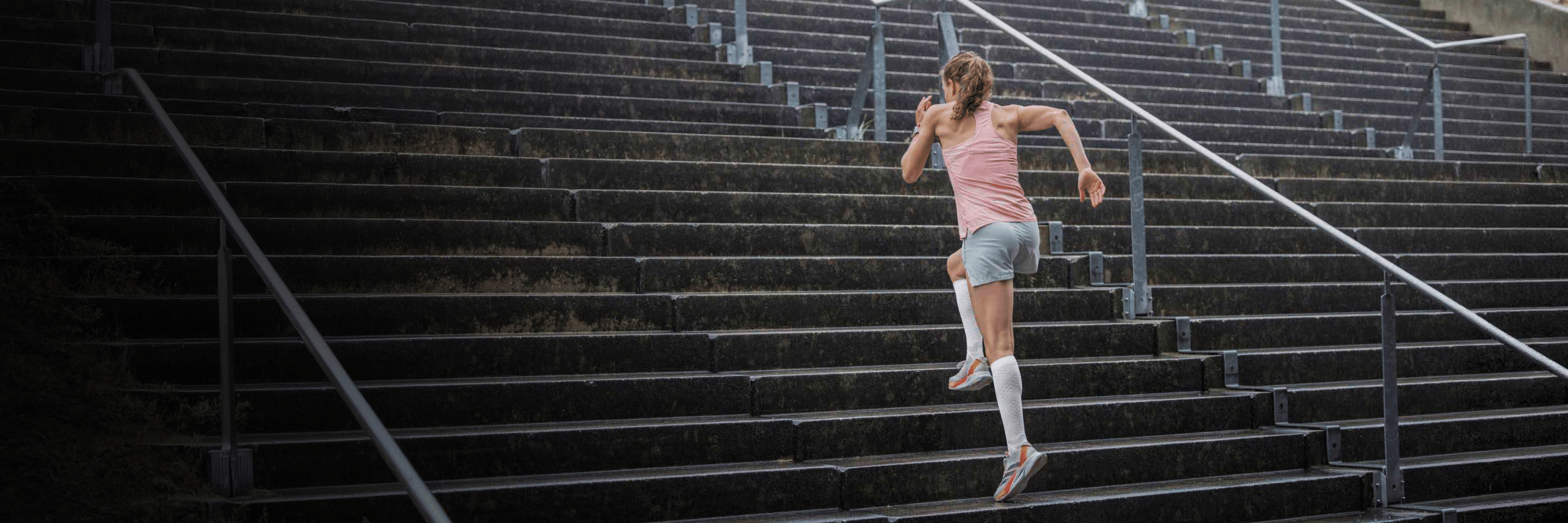 Person running up a set of outdoor stairs wearing bauerfeinds white knee high run performance compression socks in white